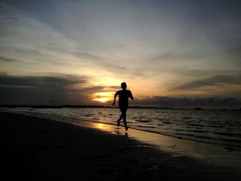 Silhouette man running on shore at beach against sky during sunset