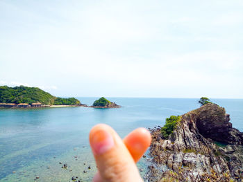 Person hand by sea against sky