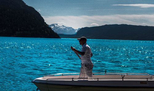 Man standing in boat on sea against mountains