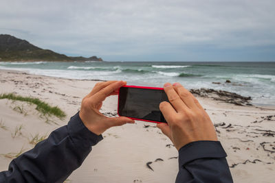 Midsection of man photographing sea with mobile phone on beach