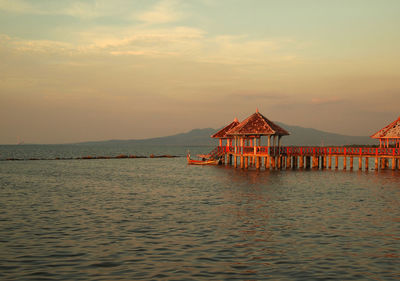 Stilt house by sea against sky during sunset