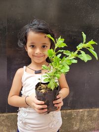 Low angle view of young girl holding plant standing against wall