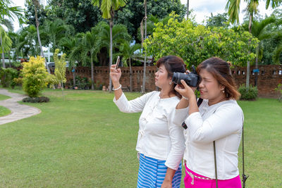 Young woman photographing with mobile phone while standing by plants