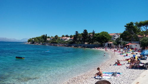 People on beach against clear blue sky