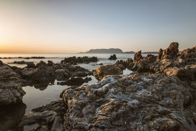 Rocks on beach against sky during sunset