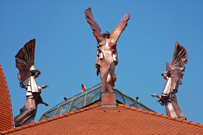 Low angle view of angel statue against building against clear blue sky