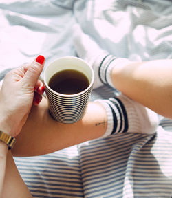 Personal perspective of woman holding coffee cup on bed