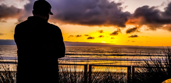 Silhouette man looking at sea against sky during sunset