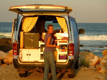 Portrait of woman holding basket while standing by van against sky