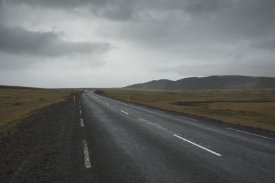 Road passing through field against cloudy sky