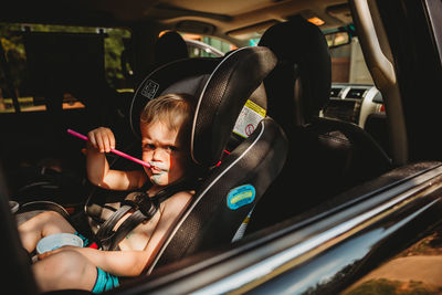 Young boy with grumpy face drinking from straw in car seat