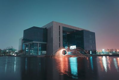 Illuminated city by river against clear sky at night