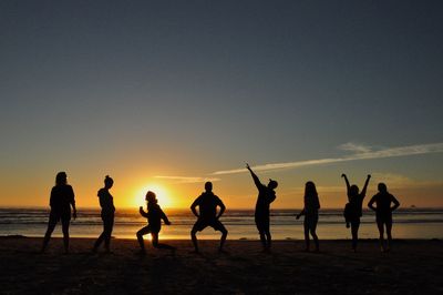 Silhouette people on beach against sky during sunset