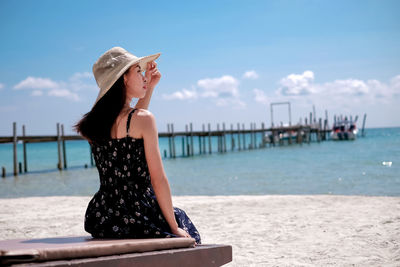 Rear view of woman wearing hat on beach against sky