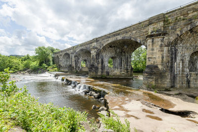 An old stone bridge, sky is densely overcast, bridge and water are illuminated by bright sunlight