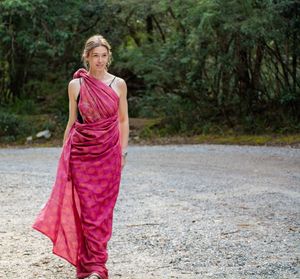 Smiling woman wearing sari walking on dirt road against plants