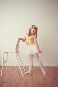 Ballet dancer standing on wooden floor against wall