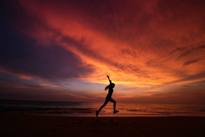 Side view of silhouette woman jumping at beach during sunset