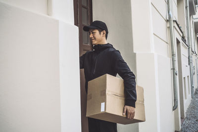 Smiling delivery man with package standing at doorstep