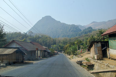 Road amidst buildings and mountains against sky