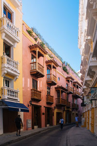 People walking on road amidst buildings against sky in city