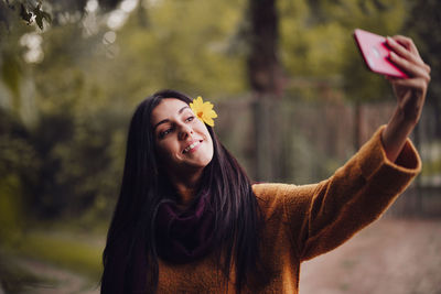 Close-up of woman taking selfie wearing flower in hair standing outdoors