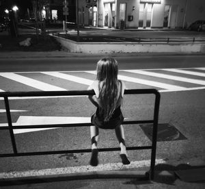 Rear view of girl sitting on railing in city