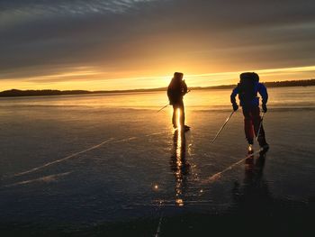 Hikers ice-skating on frozen landscape against sky during sunset