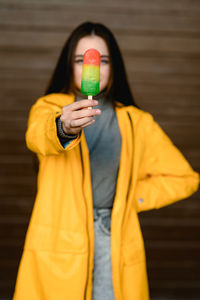 A girl in a yellow raincoat and a gray sweater holds a multicolored ice cream in her hand
