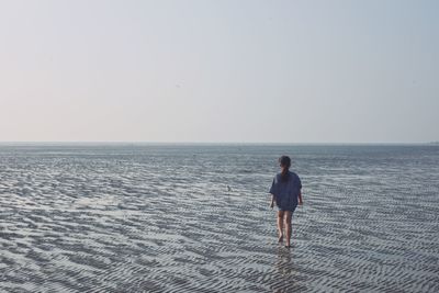 Rear view of woman on beach against clear sky