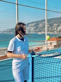 Portrait of young woman standing by chainlink fence