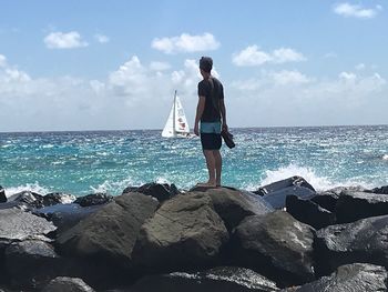 Man standing on rock by sea against sky