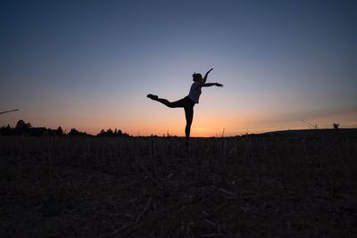 Silhouette young woman exercising on field against sky during sunset