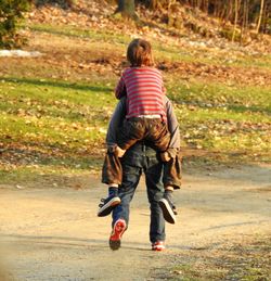 Rear view of brother piggybacking son while walking on road