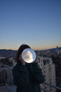 Young woman holding mirror against clear blue sky