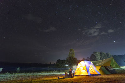 Man sitting by tent on field against sky at night