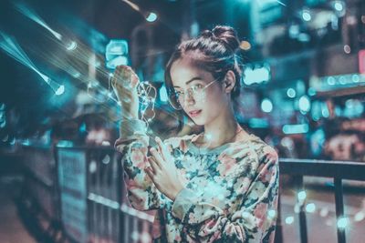 Portrait of young woman holding illuminated city at night