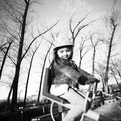 Side view of girl on play equipment against bare trees at playground