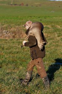 Side view of young man carrying dead deer on grassy field