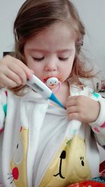 Close-up of cute girl holding thermometer while sitting at home