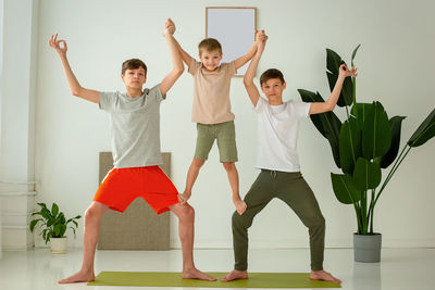 A happy boy and two teenagers perform group yoga exercises with support while sitting on a  mat.