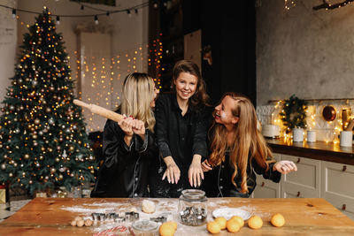 Funny girlfriends laugh and have fun cooking dough cookies at a christmas party in the kitchen