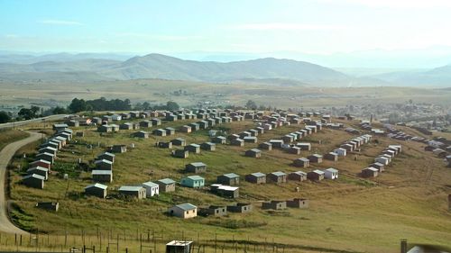 Houses on landscape by mountains against sky