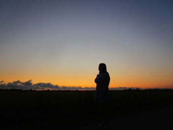 Silhouette teenage girl standing on field against sky during sunset