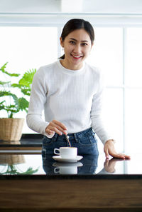 Portrait of a smiling young woman standing at table