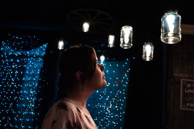 Side view of woman looking at illuminated string lights