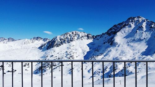 Scenic view of snowcapped mountains seen through railing against blue sky