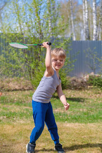 A fair-haired child plays badbinton on the lawn