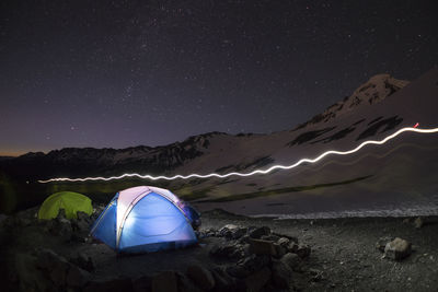 A light glows from a blue tent while stars shine above base camp mt. baker