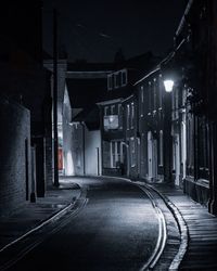 Empty street amidst illuminated buildings in city at night